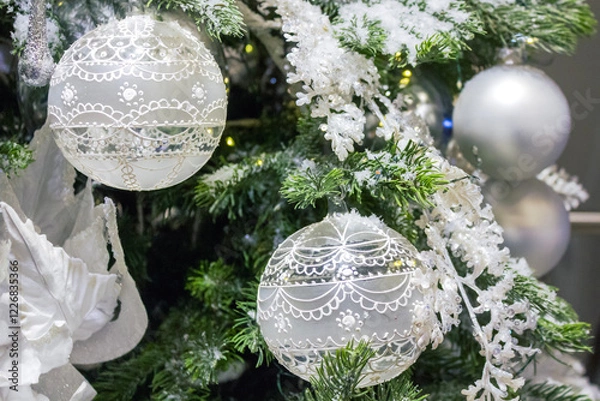 Fototapeta Close-up of a beautifully decorated Christmas tree with lace-patterned baubles and frosted foliage.