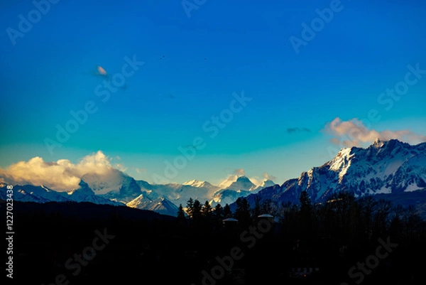 Fototapeta A breathtaking view of rugged mountain peaks bathed in dramatic light created by the Föhn storm. The warm, dry winds sweep across the alpine landscape, creating a unique atmospheric effect with swirli
