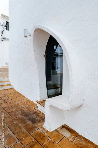 Obraz This image captures a charming architectural detail of a whitewashed building in Menorca, featuring a unique curved doorway design. Ideal for showcasing traditional Mediterranean architecture
