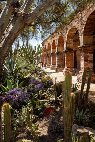 Fototapeta outdoor walkway in mission of San Juan Capistrano with desert plants in foreground