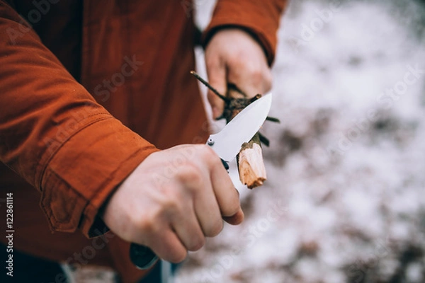 Fototapeta A man uses a knife to whittle a stick out hiking