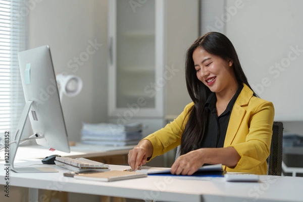 Fototapeta Professional woman in a bright office setting, organizing paperwork at her desk. She is focused and smiling, suggesting a positive work environment and efficient productivity