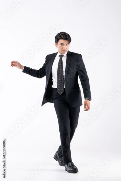 Fototapeta A man in a black suit and tie stands in front of a white background