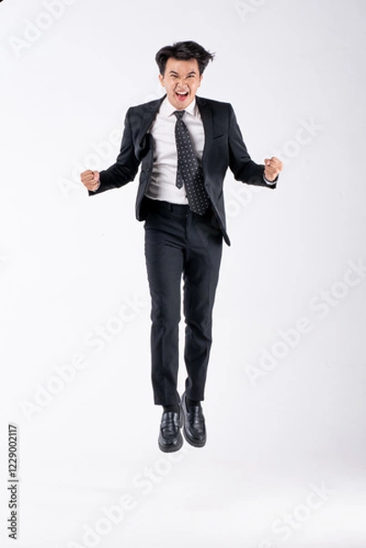 Fototapeta A man in a black suit and tie stands in front of a white background
