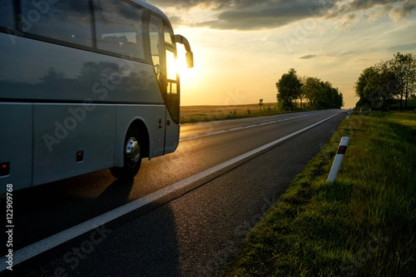 Obraz White Bus driving along the asphalt road in a rural landscape at sunset.