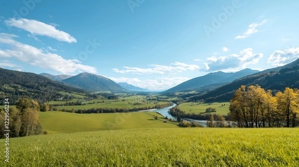 Fototapeta Scenic landscape featuring a lush green valley with a winding river and distant mountains under a clear blue sky