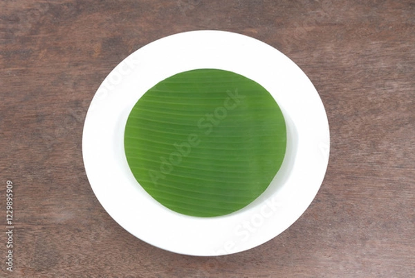 Fototapeta Ceramic plate with banana leaves in the plate on a wooden table, top view above.  Mockups can be used to edit food product displays or design layouts.