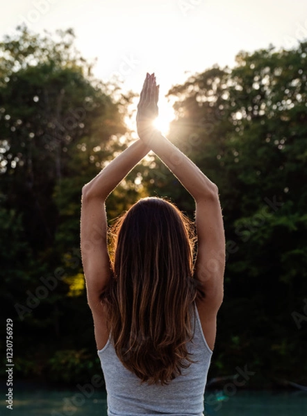 Fototapeta Back rear view of happy young woman standing at nature with hands up meeting the sun doing yoga. Harmony and connection with nature, meditation