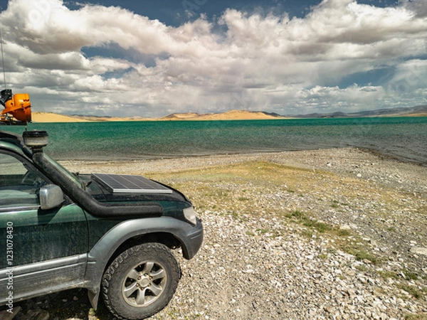 Fototapeta An off-road car with a solar panel stands against the background of dunes and a lake, overlooking the blue sky. Electric touring car with a view of Lake Barkhany and the sky. Off-road tires.