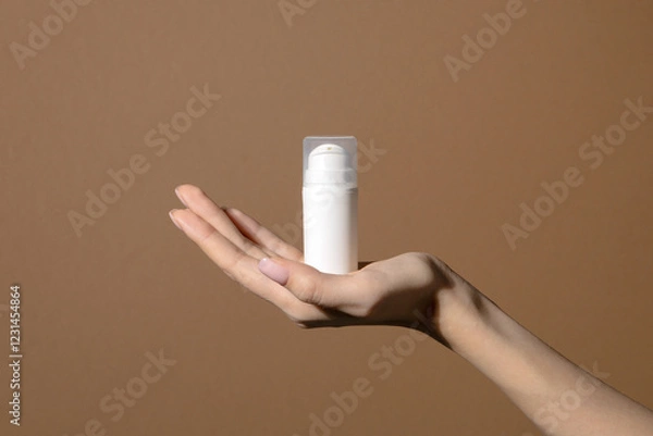 Obraz Woman's hand gently hold white bottle of unmarked cosmetics. Mockup container with dispenser for serum, lotion, cream, and retinol.