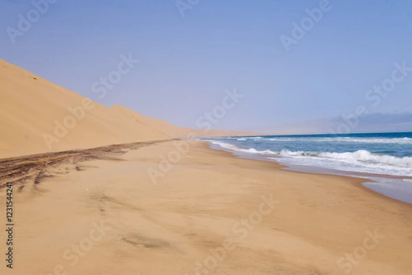 Obraz A breathtaking view of Sandwich Harbour, where golden sand dunes meet the deep blue Atlantic Ocean, creating a stunning contrast in this remote and untouched landscape.