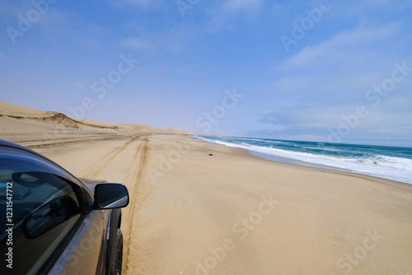 Obraz A 4x4 adventure along the wild shores of Sandwich Harbour, where vehicle tracks carve through the sand, revealing a stunning landscape where desert and ocean collide.