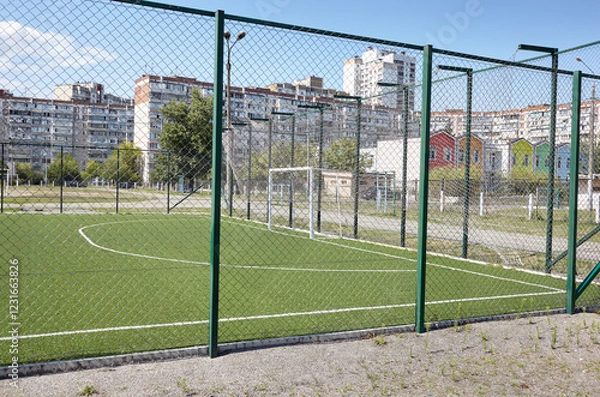 Fototapeta Lawn field for playing football behind the green fence mesh at school territory. Close-up of soccer field with green grass