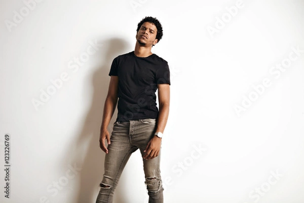 Obraz Seksowny zmysłowy ponury wyglądający African American model w pustej czarnej koszulce i obcisłych dżinsach na tle białej ściany