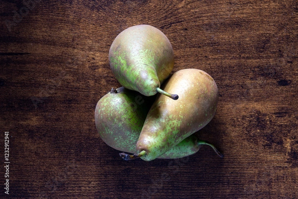 Fototapeta Three green pears are sitting on a wooden table. The pears are ripe and ready to eat