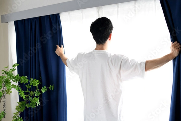 Obraz カーテンを開け日光を浴びるアジア人男性