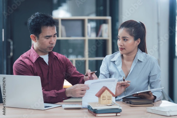 Fototapeta Real Estate Professionals: A  real estate agent and a client discuss paperwork and a model house, a professional and attentive conversation in an office setting.