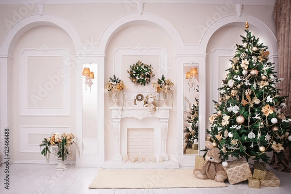 Obraz Majestic white hall with classical fireplace, arches and mirrors. At the wall Christmas wreath. New Year tree stands in the corner of room. 