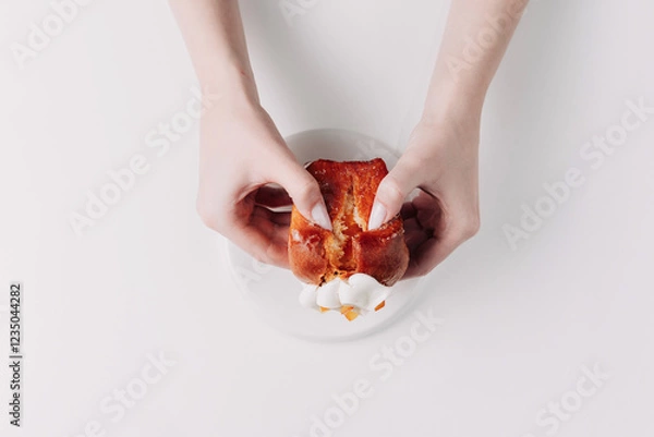 Fototapeta Woman's hands tearing, unwrapping, and crushing a pastry on a white plate against a white background