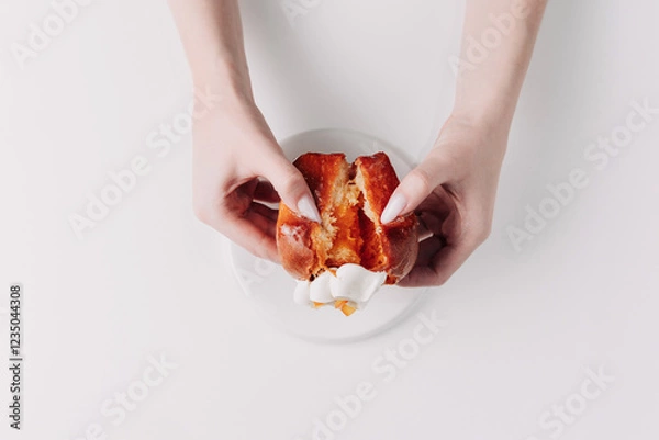 Fototapeta Woman's hands tearing, unwrapping, and crushing a pastry on a white plate against a white background