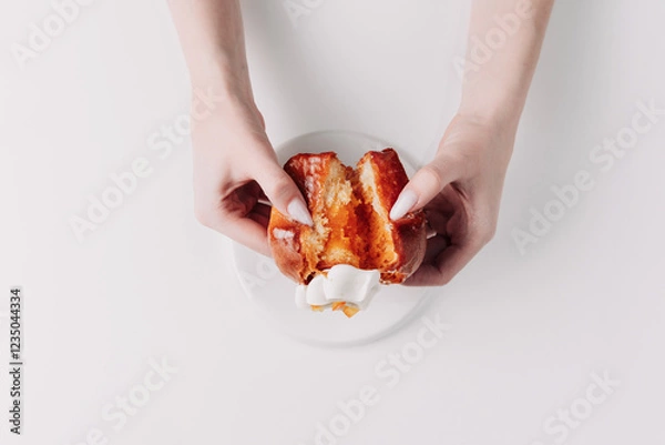 Fototapeta Woman's hands tearing, unwrapping, and crushing a pastry on a white plate against a white background