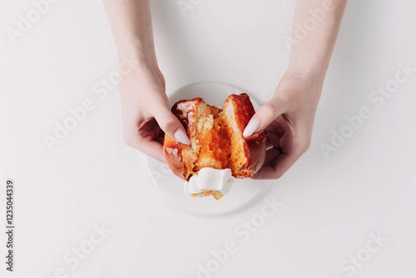 Fototapeta Woman's hands tearing, unwrapping, and crushing a pastry on a white plate against a white background