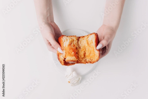 Fototapeta Woman's hands tearing, unwrapping, and crushing a pastry on a white plate against a white background