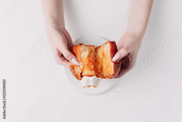 Fototapeta Woman's hands tearing, unwrapping, and crushing a pastry on a white plate against a white background