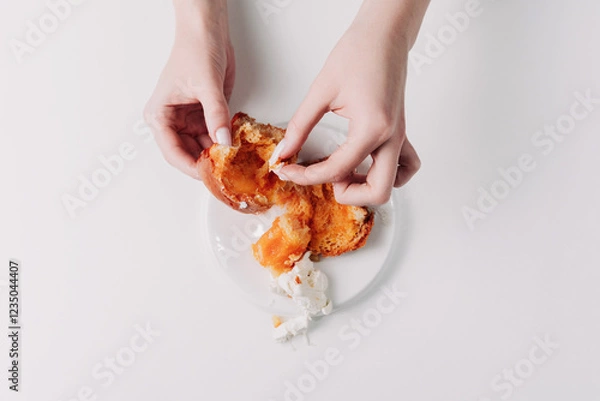 Fototapeta Woman's hands tearing, unwrapping, and crushing a pastry on a white plate against a white background