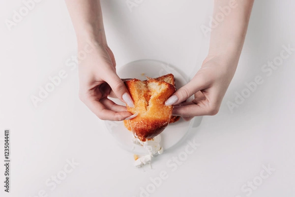 Fototapeta Woman's hands tearing, unwrapping, and crushing a pastry on a white plate against a white background