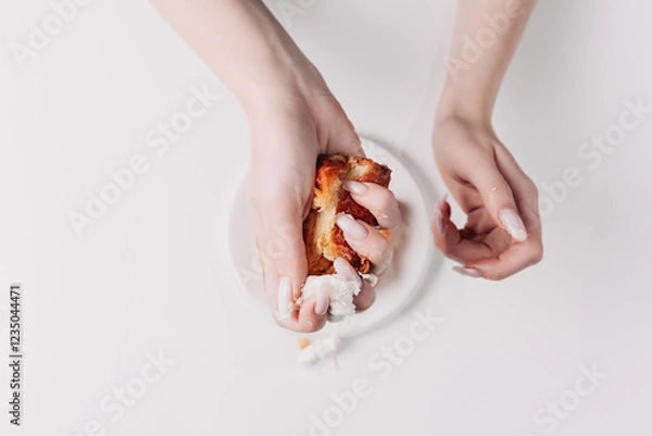 Fototapeta Woman's hands tearing, unwrapping, and crushing a pastry on a white plate against a white background