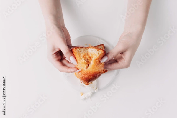 Fototapeta Woman's hands tearing, unwrapping, and crushing a pastry on a white plate against a white background