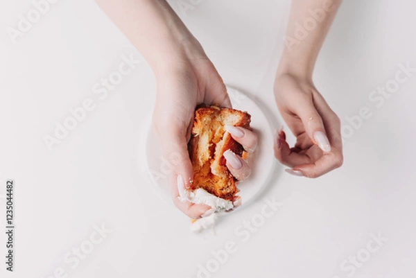 Fototapeta Woman's hands tearing, unwrapping, and crushing a pastry on a white plate against a white background