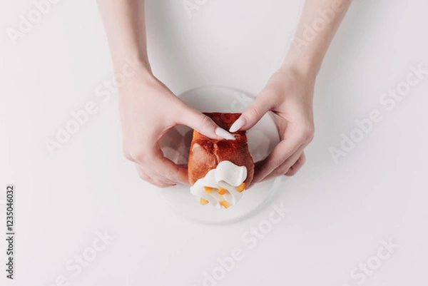 Fototapeta Woman's hands tearing, unwrapping, and crushing a pastry on a white plate against a white background