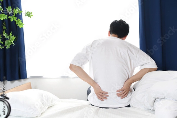 Fototapeta ベッドの上で腰を抑える若い男性の後ろ姿