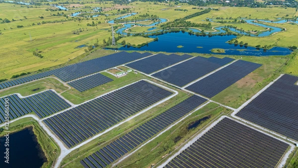 Fototapeta Drone shot aerial view solar energy array provides renewable power in large scale facility surrounded by greenery and water in rural place. Solar farm at the countryside