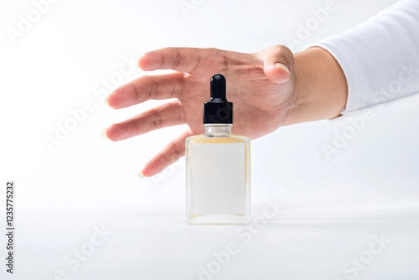 Obraz A hand reaches towards a clear dropper bottle on a plain white surface, emphasizing simplicity and elegance in design