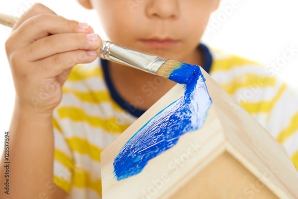 Obraz Child paints wooden birdhouse on a white background