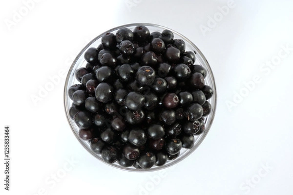 Obraz Fresh aronia berries in a glass bowl, white background, top view