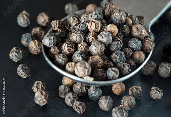 Obraz Raw organic black peppercorns or Dry black pepper seeds in stainless steel spoon on black background. use it as your Space for text, Design, Wallpaper and Poster, Selective focus.
