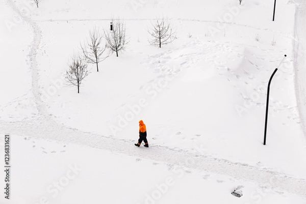 Fototapeta Worker in an orange jacket standing on a snowy path in winter, top-down view