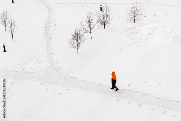 Fototapeta Worker in an orange jacket standing on a snowy path in winter, top-down view