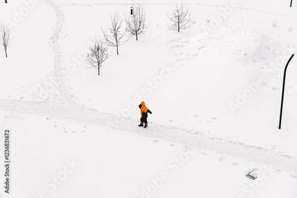 Fototapeta Worker in an orange jacket standing on a snowy path in winter, top-down view