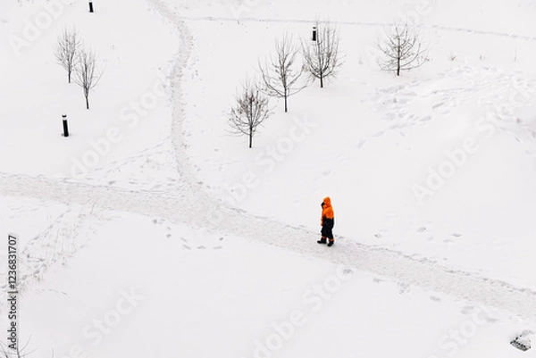 Fototapeta Worker in an orange jacket standing on a snowy path in winter, top-down view