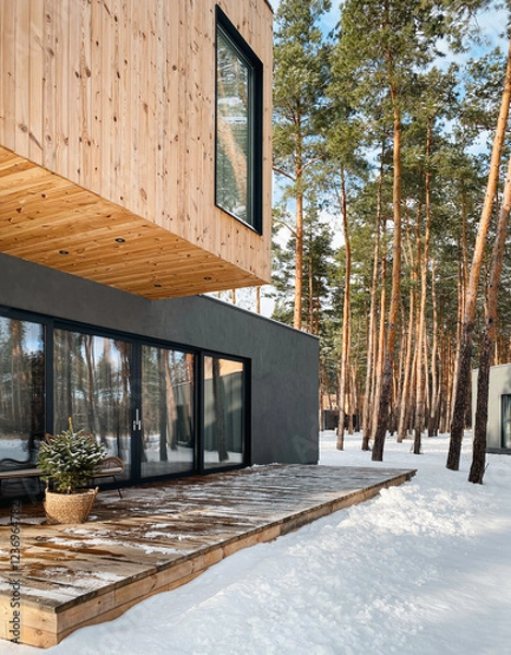 Obraz Two-storey timber-clad house in pine forest on a sunny day. Modern house with porch in winter forest. 