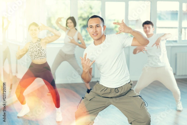 Fototapeta Positive smiling young man dancing hip hop with group of guys and girls in modern dance class