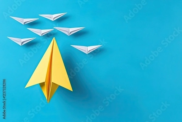 Fototapeta A vibrant yellow paper airplane leads a group of white paper airplanes, symbolizing creativity and innovation against a bright blue background.