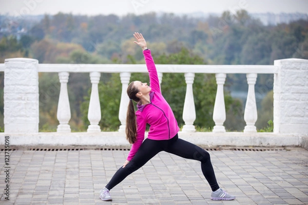 Fototapeta Sporty beautiful smiling young woman practicing yoga, standing in Reverse Warrior Pose, Viparita Virabhadrasana, working out outdoor on summer day wearing sportswear sweatshirt. Full length, side view