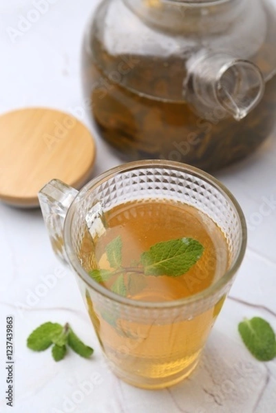 Fototapeta Aromatic mint tea and fresh leaves on white textured table, closeup