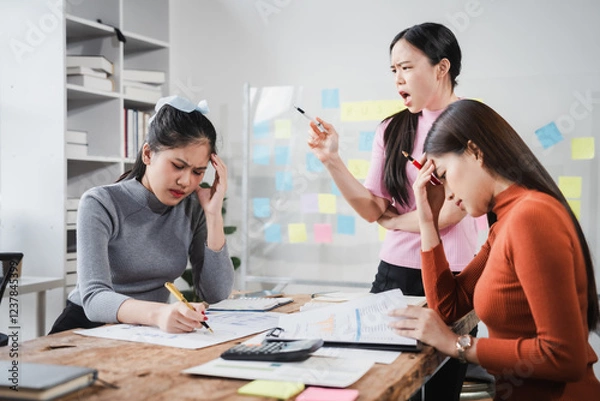 Obraz Asian people, frustrated businesswoman sits at desk, grappling with challenges of her startup, acknowledging failure, and seeking ways to learn and grow. team meeting. blamed